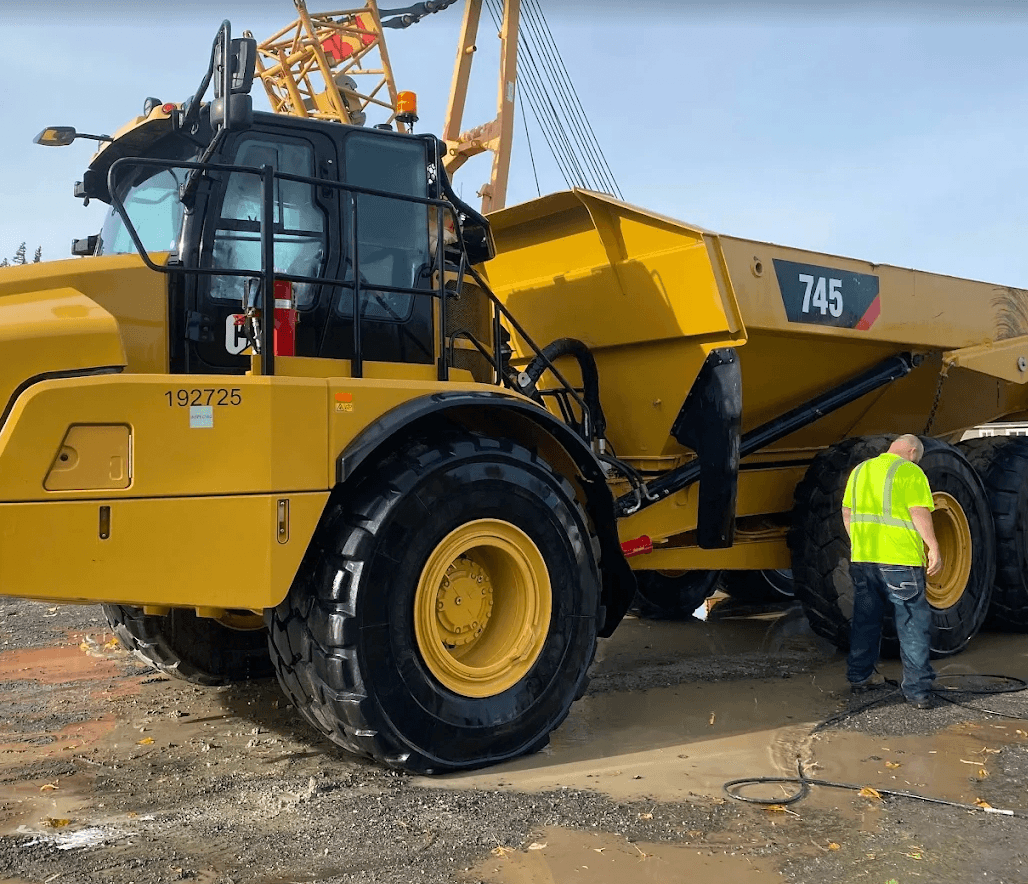 Large yellow Caterpillar 745 articulated dump truck on muddy ground with a nearby worker.