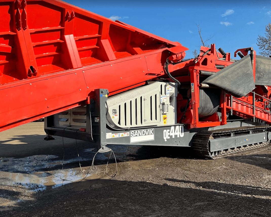 Red Sandvik QE440 heavy-duty mobile scalping screen on tracks against a clear blue sky.
